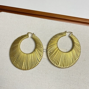 Vue détaillée de grandes boucles d'oreilles dorées avec motifs radiaux texturés