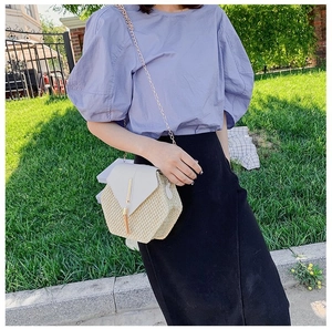 Detailed view of woven straw shoulder bag with white leather flap and tassel chain strap