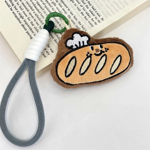 Detail of plush bread keychain featuring a white chef hat and green spring hook on a book
