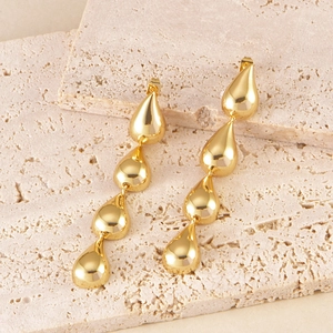Macro shot of gold teardrop tassel earrings cascading on a natural stone surface