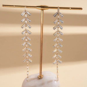 Detail view of long gold tassel earrings featuring cascading baguette-cut crystals on a stand