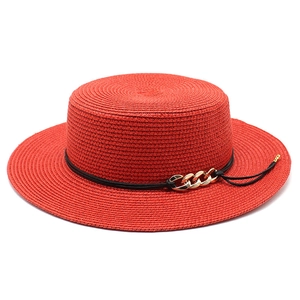 Détail d'un chapeau canotier rouge en paille avec chaîne dorée et texture tissée fine