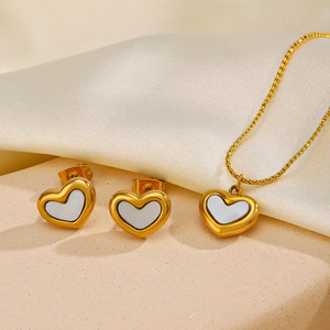 Elegant gold shell heart necklace and earrings set on beige stone and silk background