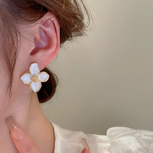 Nahaufnahme eines weißen Blumenohrrings mit goldenem Rand, getragen von einem Model