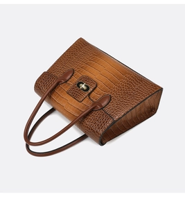 Detailed view of brown crocodile texture leather and golden metal rotary lock on handbag