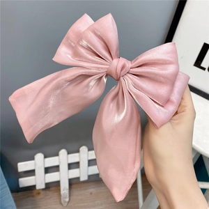 Close-up of a large pearlescent pink bow hair clip showing the layered satin fabric texture