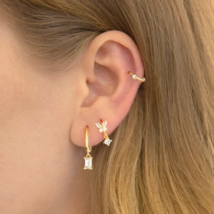 Close-up of gold hoop earrings with zircon rectangle and butterfly charms worn on ear