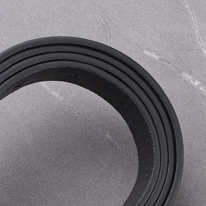 Detail of classic black leather belt showing textured surface and round buckle on marble