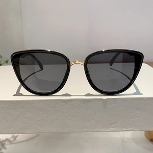Close-up of cat-eye sunglasses with dark grey lenses and gold metal hinge details