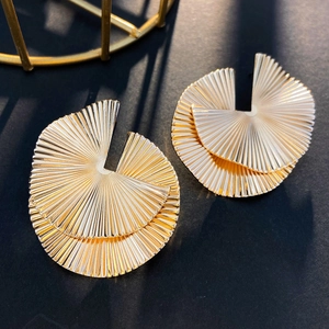 Detail of fan-shaped golden metal earrings with fine radial pleated textures