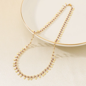 Detail of gold chain necklace with purple beads and drop pendants on ceramic tray