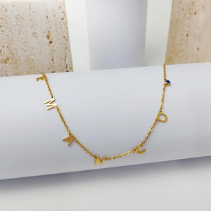 Detalle de un collar dorado con colgantes de letras y una pequeña piedra preciosa azul
