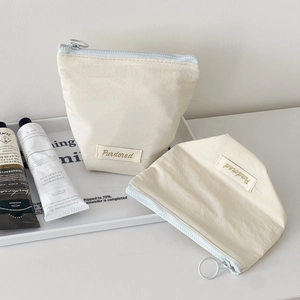 Detail of cream fabric makeup bag with blue zipper and round metal ring puller