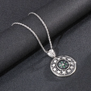 Macro detail of silver nautical compass pendant with embossed star pattern on rope chain