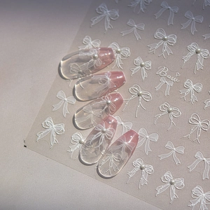 Detailed view of white bow nail stickers with pearls on pink gradient false nails