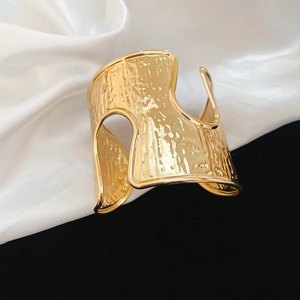 Detail of gold-colored open cuff bracelet featuring artistic hammered metal texture