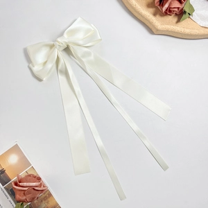 Detail of cream white satin bow hair clip with long ribbons on an elegant background