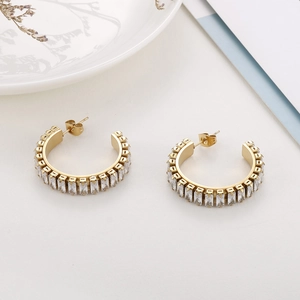 Detail of gold C-shaped hoop earrings featuring rectangular white zircon stones