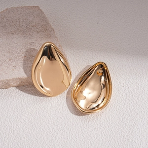 Detail of high-polished gold teardrop earrings on a minimalist stone background