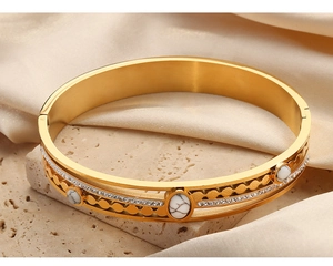 Detailed macro of gold plated hollow bangle with turquoise stones on marble and silk