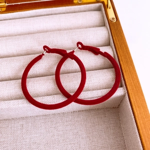 Macro shot of red flocked round hoop earrings with silver pins in a wooden jewelry box