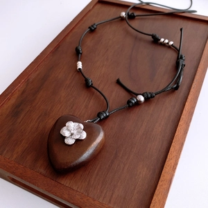 Close-up of heart-shaped wooden pendant with silver floral detail on a rustic wood tray