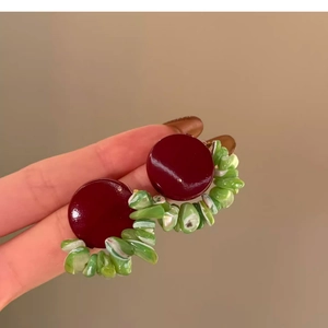 Detail of geometric round acrylic shell earrings featuring red and green resin stones