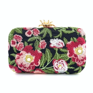 Close-up of elegant floral embroidery and pearl-topped crown clasp on black evening bag