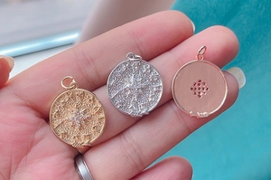 Detailed close-up of gold, silver, and rose gold coin pendants with embossed compass designs