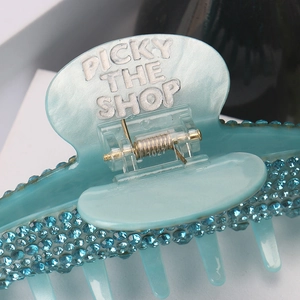 Detail shot of large blue resin hair claw clip with rhinestones and brand lettering