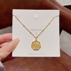 Detailed close-up of golden octagonal flower pendant on fine bead chain with display card