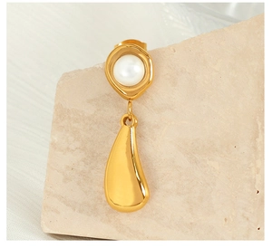 Close-up of golden teardrop earring with white pearl on natural stone background