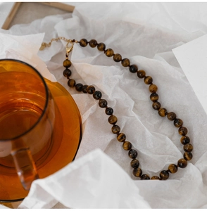 Macro detail of tiger eye stone necklace with gold clasp on textured background