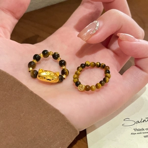 Detailed macro view of tiger eye bead rings with golden cat charm on hand display