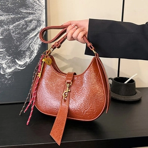 Detail of dark brown pleated shoulder bag with heart pendant and woven rope accessory