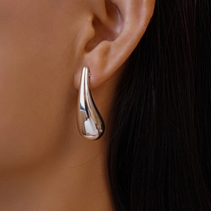 Macro shot of polished silver teardrop earring showing smooth metallic finish on ear