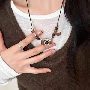 Detailed view of retro camera pendant necklace with wooden beads on a brown sweater