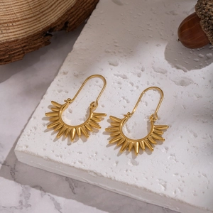 Macro shot of gold sunburst earrings on stone, showing detailed U-hook and metallic texture