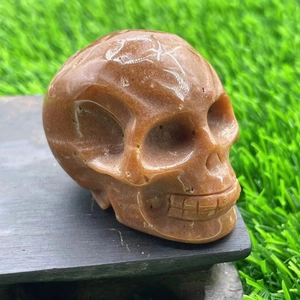 Detailed macro shot of a hand-carved 5cm brown crystal skull on a lush green lawn