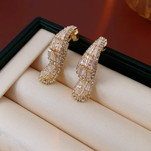 Macro shot of gold teardrop earrings with shimmering zircons on a leather box