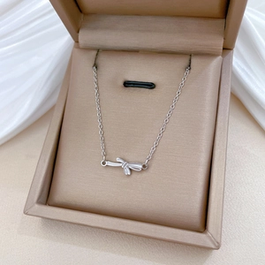 Close-up of a silver bow necklace in a jewelry gift box on white satin fabric