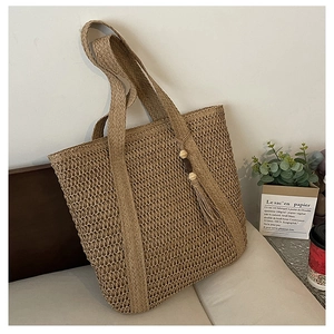 Detail of hand-woven straw tote bag with wood bead tassel on a cozy light chair