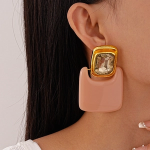 Close-up of geometric gold-framed rectangle earrings with peach resin and clear crystal