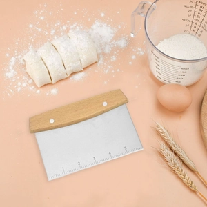 Stainless steel dough scraper with wooden handle and scale markings on pink background