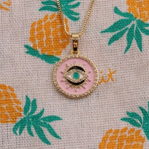 Gros plan du collier pendentif œil maléfique doré avec émail rose et pierre précieuse verte