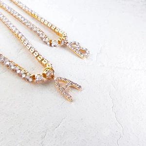 Close-up of golden tennis chain necklaces with A and B initial pendants set in zircon