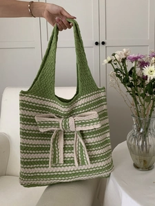 Detail view of a green and beige striped knitted tote bag with a large decorative bow