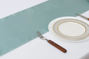 Detail of teal satin table runner with hemmed edges and elegant glossy texture on a table