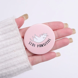 Pink tinplate badge with a white cat and Stay Pawsitive quote on a white sweater