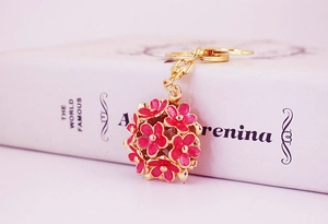 Detail of rose red enamel daisy ball keychain with golden finish and floral pattern